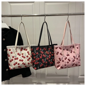 Trois sacs cabas imprimé cerises en crème, noir et rose suspendus sur un support