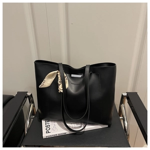 Dettaglio di una borsa tote in pelle nera con foulard floreale su una sedia chic