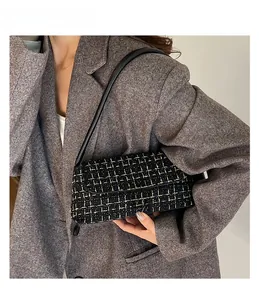 Detail of black and gold tweed underarm bag featuring a metallic turn-lock closure