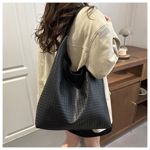 Detail view of black woven texture shoulder bag worn by model in a cozy indoor setting