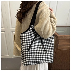 Detail of a large black and white gingham tote bag with black ribbon on a shoulder model