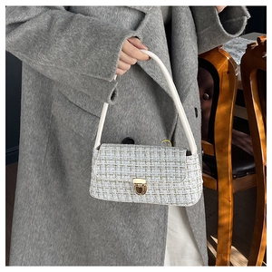 Detail of tweed crossbody bag featuring light blue patterns and gold rotating metal clasp