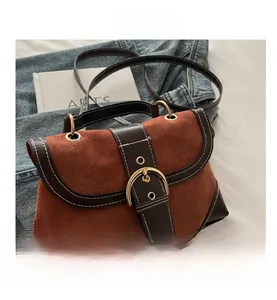 Detail of brown suede and leather handbag featuring contrast stitching and large gold buckle