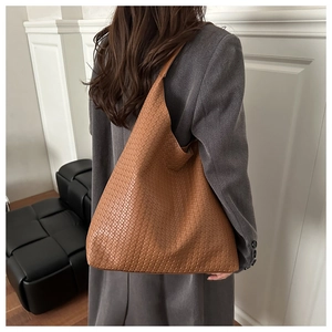 Detail of a brown woven leather tote bag with Intrecciato pattern on a female model