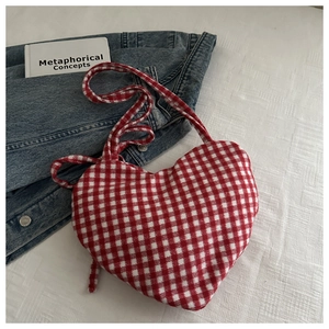 Detail van een hartvormige rood-wit geruite crossbodytas op een witte stoffen ondergrond