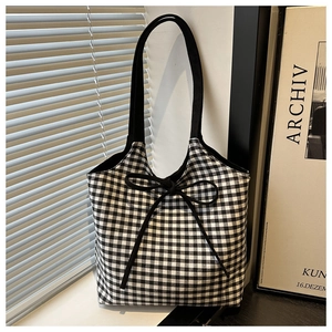 Detail of checkered canvas tote bag with black bow tie and wide woven shoulder strap