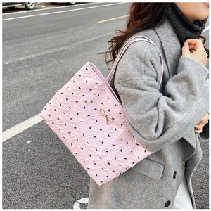 Pink tote bag with black bow patterns and gold pendant shown on model's shoulder