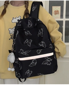 Detail of butterfly print backpack featuring reflective strip and white plush ball charm
