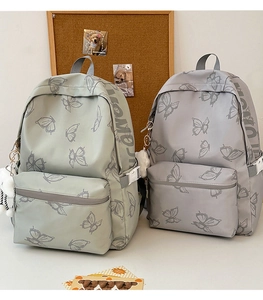 Detail view of butterfly print backpacks in light green and grey with plush charms