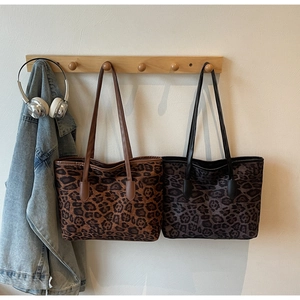 Detail view of large leopard print tote bags in brown and grey hanging on a wooden rack