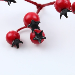 Macro shot of artificial red Christmas berries with black star-shaped caps on a stem