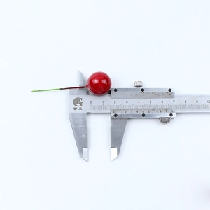 Close-up of 15mm red artificial berry with green wire stem measured by a caliper
