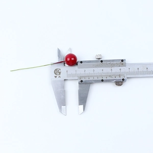 Detail view of red artificial berries measured with a caliper showing 12mm diameter size