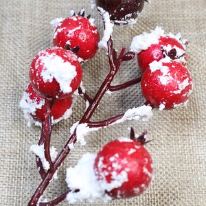 Detailed view of artificial red holly berries with thick snow texture and rustic burlap background