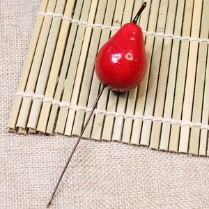Detail of a bright red artificial pear decoration with a glossy finish and long stem