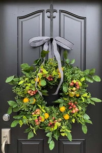 Detail of artificial greenery wreath with yellow citrus and striped ribbon on black door