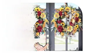 Detail of sunflower and peony wreath featuring lush greenery and black striped ribbon bow
