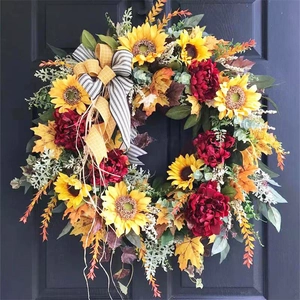 Detail of sunflower and red peony wreath with autumn leaves and striped bow on black door
