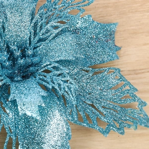 Blue glitter poinsettia flower with hollow feather edges on a wooden surface