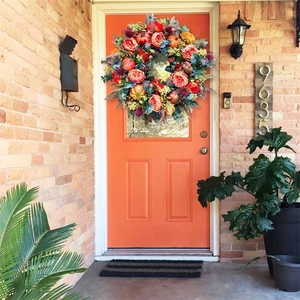 Detail of autumn wreath with pumpkins and roses hanging on a bright orange front door