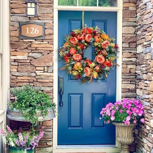 Close-up of autumn pumpkin wreath with orange roses and berries on a dark blue door