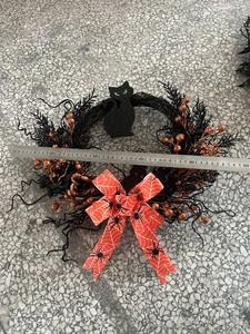 Halloween wreath detail with black cat, orange berries and spider web bow on a ruler