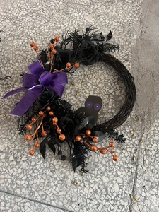 Detail of Halloween wreath with black roses, purple bow, and glowing owl silhouette