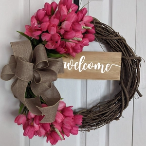 Detail of rustic floral wreath with pink tulips, burlap bow and welcome wooden sign