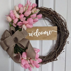 Detail of tulip wreath featuring a large burlap bow and a wooden welcome sign on a white door