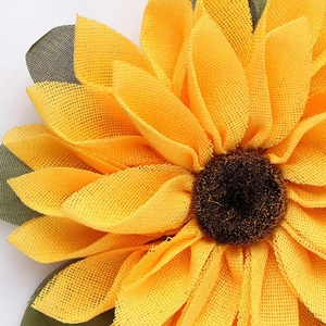 Close-up of yellow burlap mesh sunflower wreath with realistic brown center and green leaves