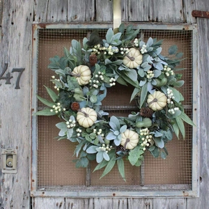 Autumn white pumpkin wreath with eucalyptus leaves and pine cones on a rustic wooden door
