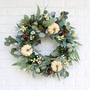 Autumn wreath with white pumpkins pine cones and green foliage on white brick wall