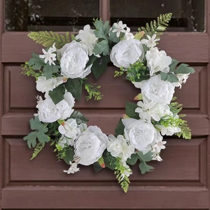 White artificial rose wreath with green leaves hanging on dark wood door for wedding decor