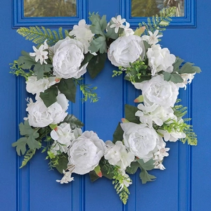 Detail of white artificial peony wreath with green leaves on a blue wooden door