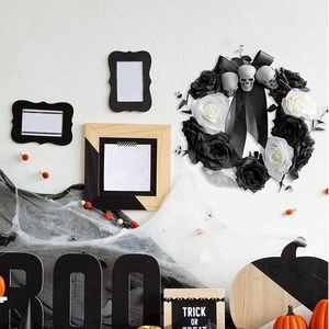 Halloween wreath with black and white faux roses and skulls on a white background wall