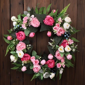 Detailed top view of silk peony wreath with green leaves and berries on wooden background