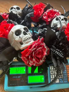 Halloween skull wreath with red glitter roses showing weight of 323.5g on a scale