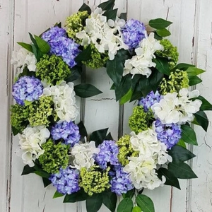 Round artificial wreath with purple and white hydrangeas on a rustic white wooden door