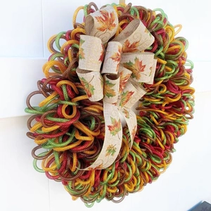 Close-up of autumn mesh wreath featuring orange maple leaf print burlap bow on white wood