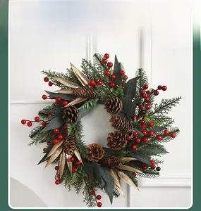 Detail of Christmas wreath with pine cones, red berries and golden leaves on white wall