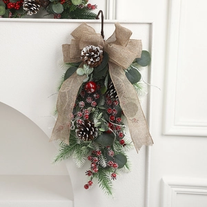 Artificial Christmas teardrop swag with red berries and pinecones on white wall