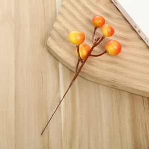 Artificial berry branch with frosted orange berries on light wood table for home decor