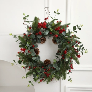 Artificial Christmas wreath with pine needles, red berries and cones on white fireplace