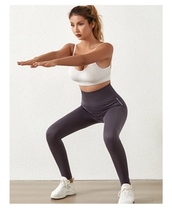 Detail van het shapende effect en merklogo op de paarse yoga legging met hoge taille