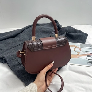 Detail of burgundy saddle bag showing woven texture flap and gold hardware accents