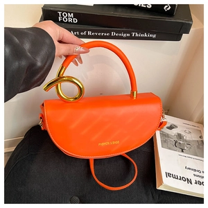 Detail of bright orange saddle bag featuring a bold gold twisted ring handle connection