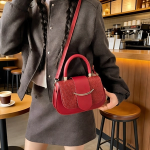 Red leather crossbody bag with woven texture lid and gold hardware in a cafe setting