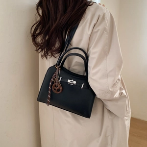 Chic black Kelly-style handbag in matte leather with silver lock, shown on a beige trench coat