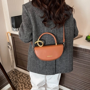 Brown leather saddle bag with golden twist metal decor and crossbody strap shown on model
