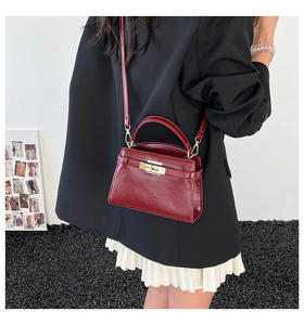 Détail d'un sac à main en cuir bordeaux avec fermoir doré porté par un mannequin